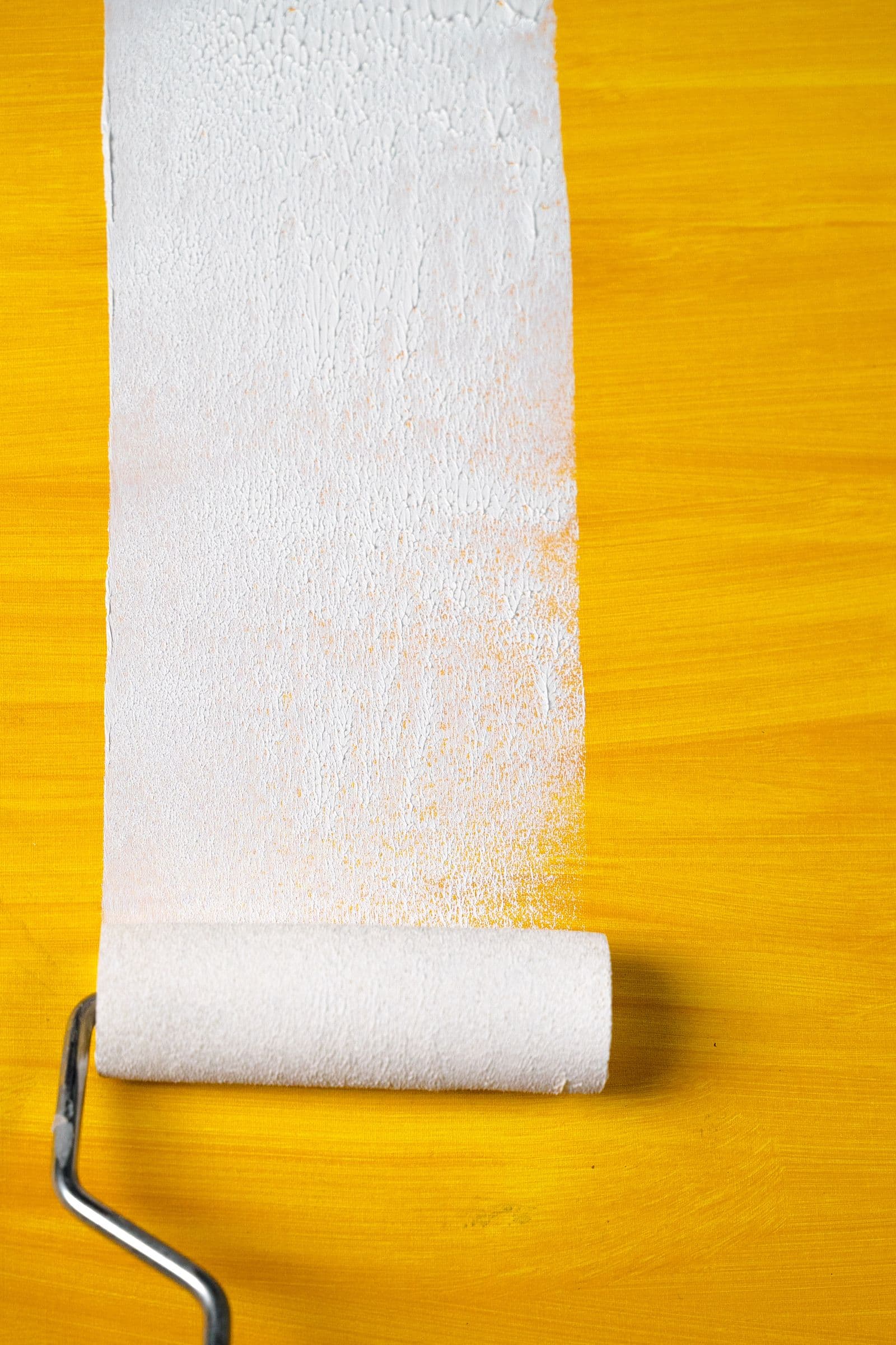 Paint roller covering a yellow wall with white paint